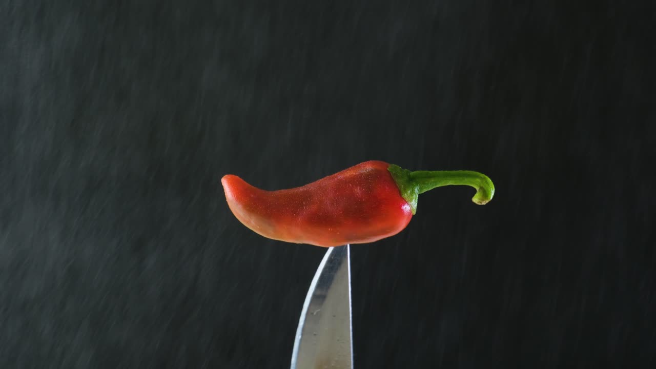 A red jalapeno chili on a knife being delicately misted until it's covered by a few drops of water