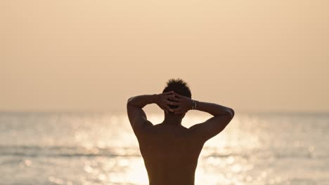 a solitary man stands on a pristine beach in the maldives, gazing at the vibrant sunset over the calm ocean.