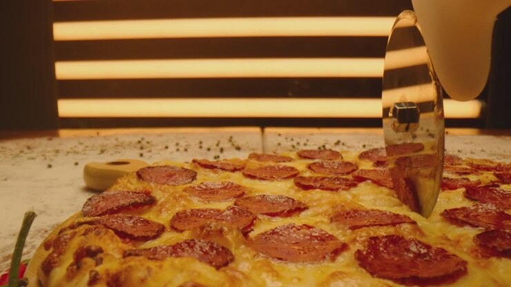 Tagliare la pizza con una rotella tagliapizza. Primo piano di una deliziosa pizza tagliata a pezzi. Pizza cotta con salsiccia, formaggio fuso, peperoni rossi. Ripreso con ARRI ALEXA e obiettivo Laowa. Movimento della telecamera.