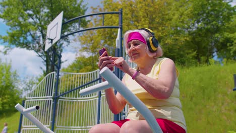 Mujer-Mayor-Después-Del-Entrenamiento-Deportivo-Escuchando-Música-En-El-Patio-De-Recreo,-Celebra-La-Victoria-Haciendo-Un-Gesto-De-Ganador