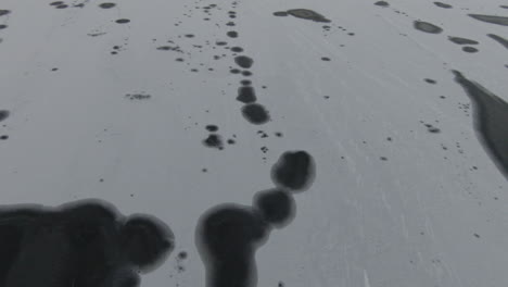 tilt down, dark abstract spots on frozen lake