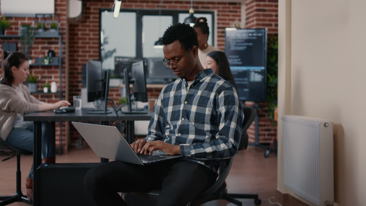 Portrait of african american programer sitting down working on laptop arranging glasses