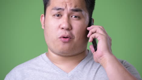 young handsome overweight asian man against green background