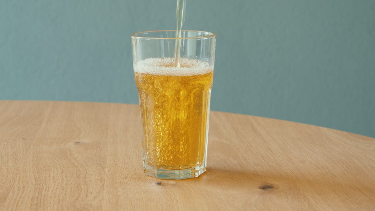 Primo piano di tè freddo versato in un bicchiere su un tavolo di legno. Concetto di bevande zuccherate, rinfresco, bevande analcoliche e consumo quotidiano di bevande.