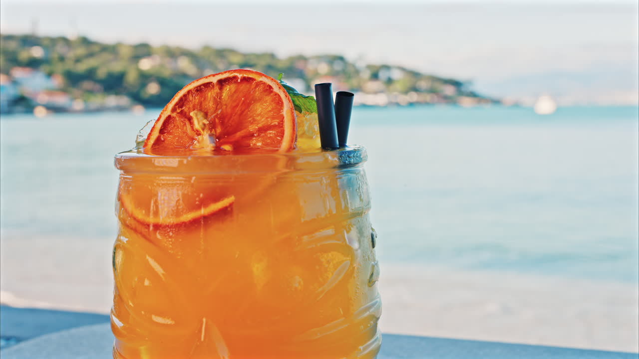 Close up of an orange cocktail on a table with a blurred view of the sea on the background