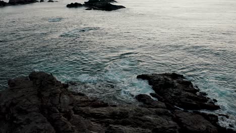 Aerial-view-rotating-shot-over-a-rock-formation-off-the-coast-of-southern-Mexico-close-to-Mazunte-with-waves-crashing-on-at-sunset