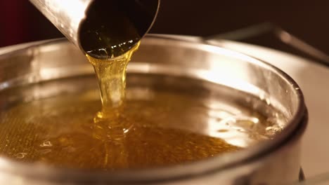 Extreme-close-up-of-fresh-healthy-honey-bee-poured-from-metal-pipe-in-a-jar