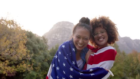 portrait of happy diverse female friends holding flag of usa and celebarting in garden, slow motion