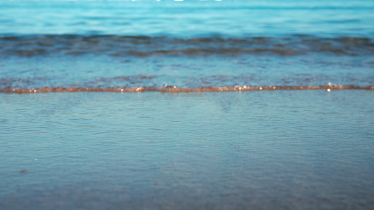 Close up of small waves rolling gently onto the sandy beach under morning light