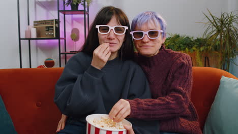 mujeres sentadas en el sofá comiendo palomitas de maíz y viendo interesantes series de televisión, juegos deportivos en línea en casa