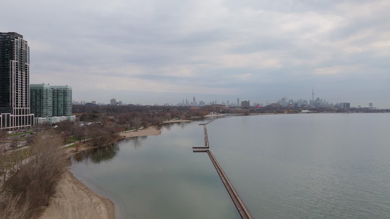 Aerial: Lake Ontario, condo buildings and CN Tower with cityscape of downtown Toronto during the day in Ontario, Canada, crane up drone shot