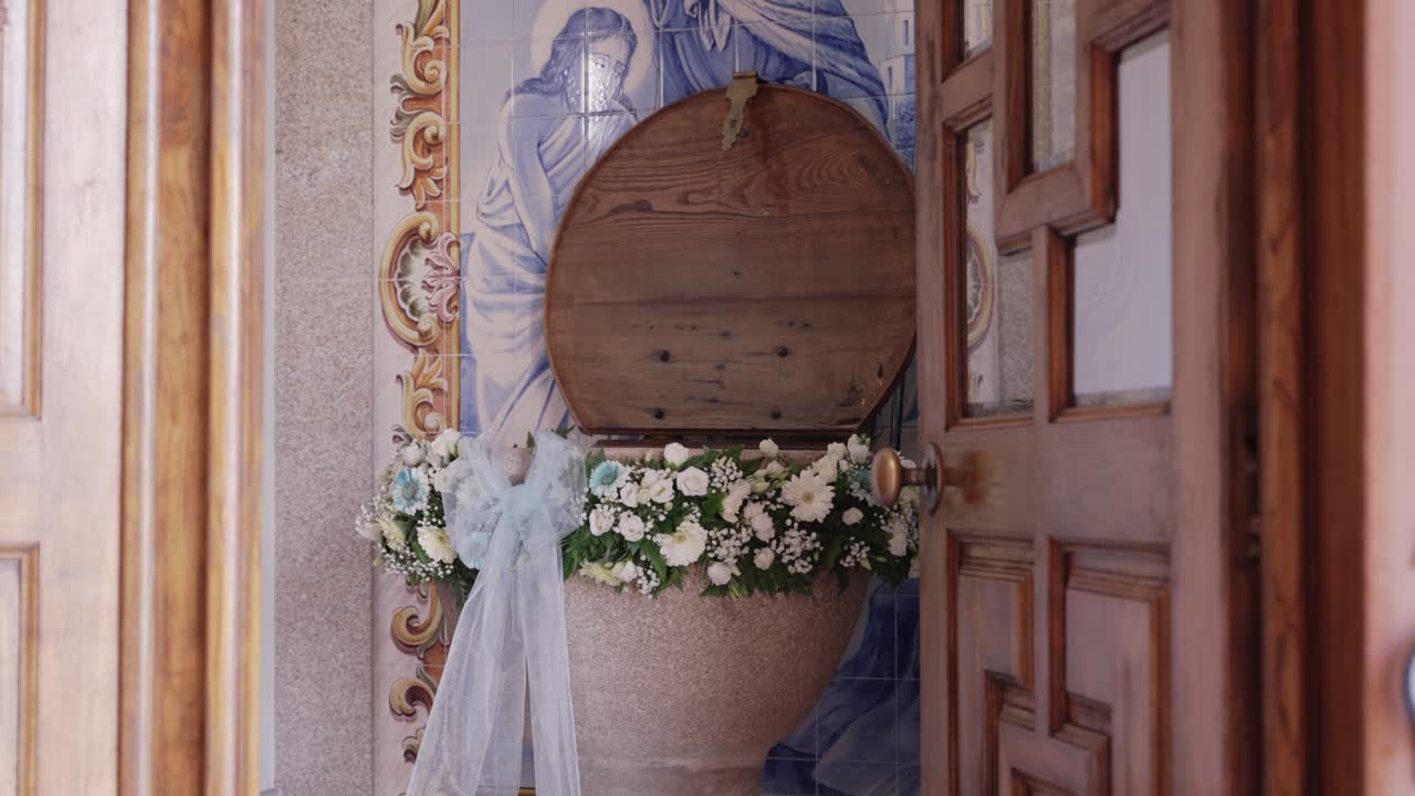 Stone baptismal font with wooden lid and floral decoration beside open church door