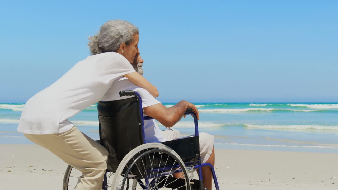 Side view of active senior African American woman embracing disabled senior man on the beach 4k