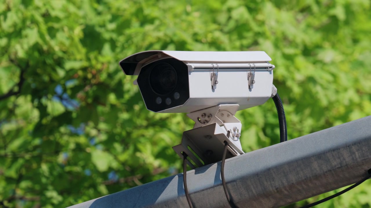 Telecamera di sorveglianza esterna montata su una struttura metallica con fogliame verde sullo sfondo