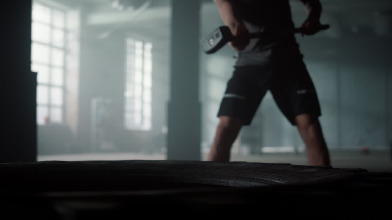 집중된 남자가 망치로 큰 타이어를 때리고 있습니다. 보디빌더는 스레지햄을 사용합니다.