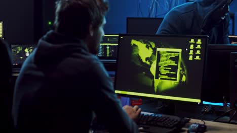 couple of young man and woman, software developers or cyber criminals working at the computers and guy coming to help them