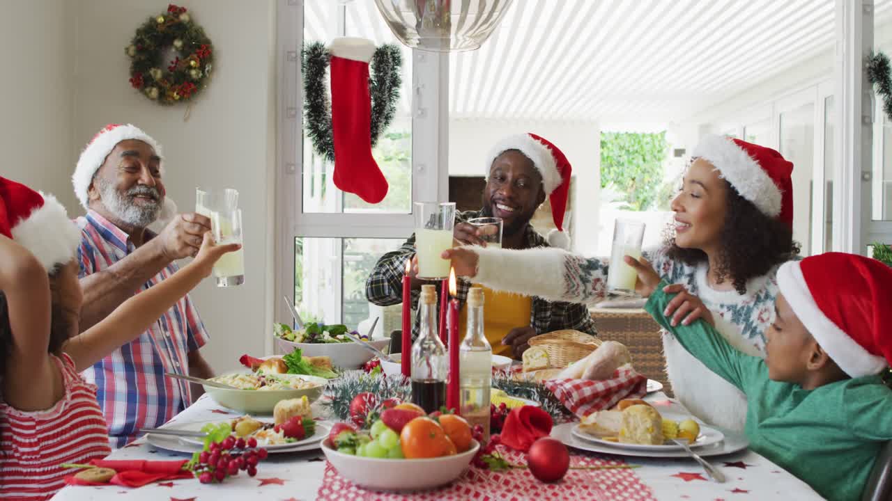 feliz familia afroamericana de varias generaciones con sombreros de papá noel y celebrando la comida navideña