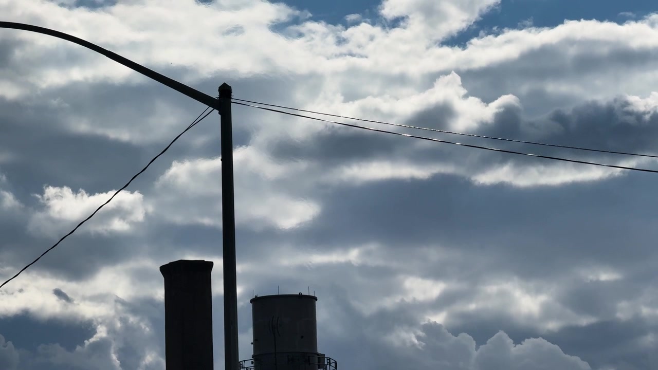 Ciminiere industriali e torre dell'acqua stagliate contro un cielo nuvoloso e drammatico.