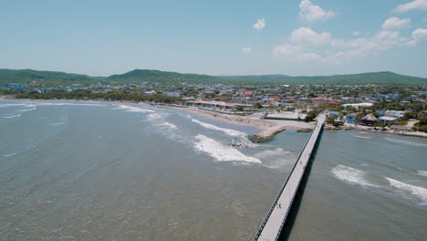 Aerial-city-view-over-Puerto-Colombia-Dock,-where-the-rhythmic-waves-meet-urban-charm