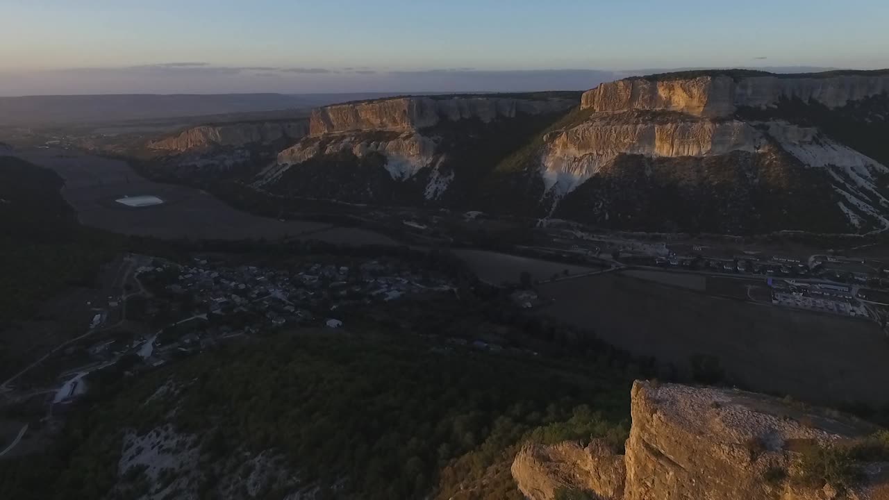 puesta de sol sobre un valle con acantilados y un pueblo