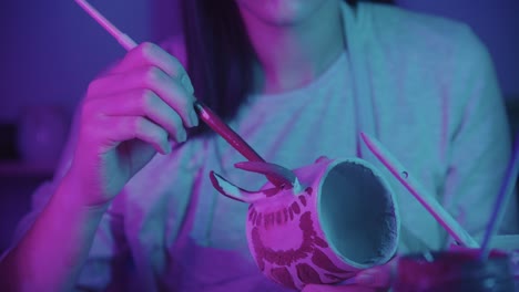 joven ceramista pintando en la taza de cerámica con un pincel en un estudio de arte - iluminación de neón