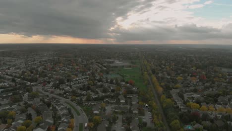 aerial footage going left over some train tracks which run through the middle of two sub-divisions and lead towards a huge sunset in autumn