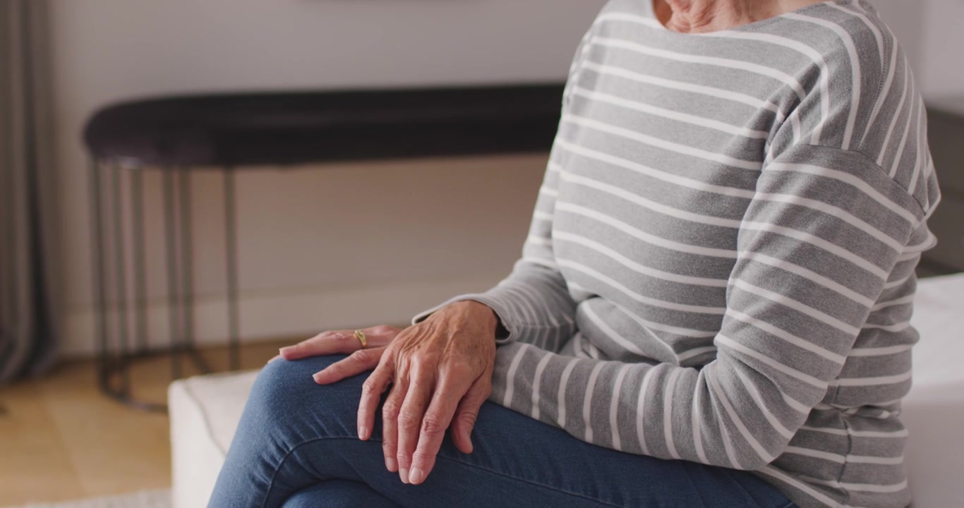 La telecamera si allontana, una donna anziana con un top a righe abbassa il mento, incrocia le gambe e si sistema con calma.
