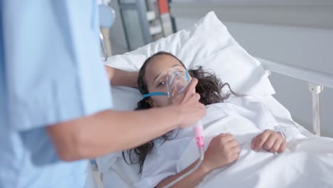 Diverse-female-doctor-and-child-patient-using-oxygen-mask-in-corridor-at-hospital,-in-slow-motion