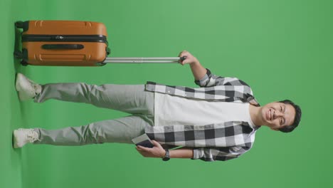 full body of asian male traveler with luggage holding passport and smiling to camera while standing in the green screen background studio