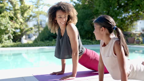 happy biracial mother and daughter practicing yoga in sunny garden, copy space, slow motion