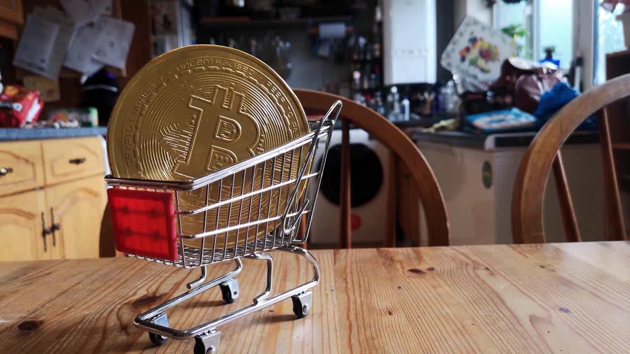 Monete di criptovaluta Bitcoin dorate in un minuscolo carrello della spesa su un tavolo da cucina, dolly a sinistra