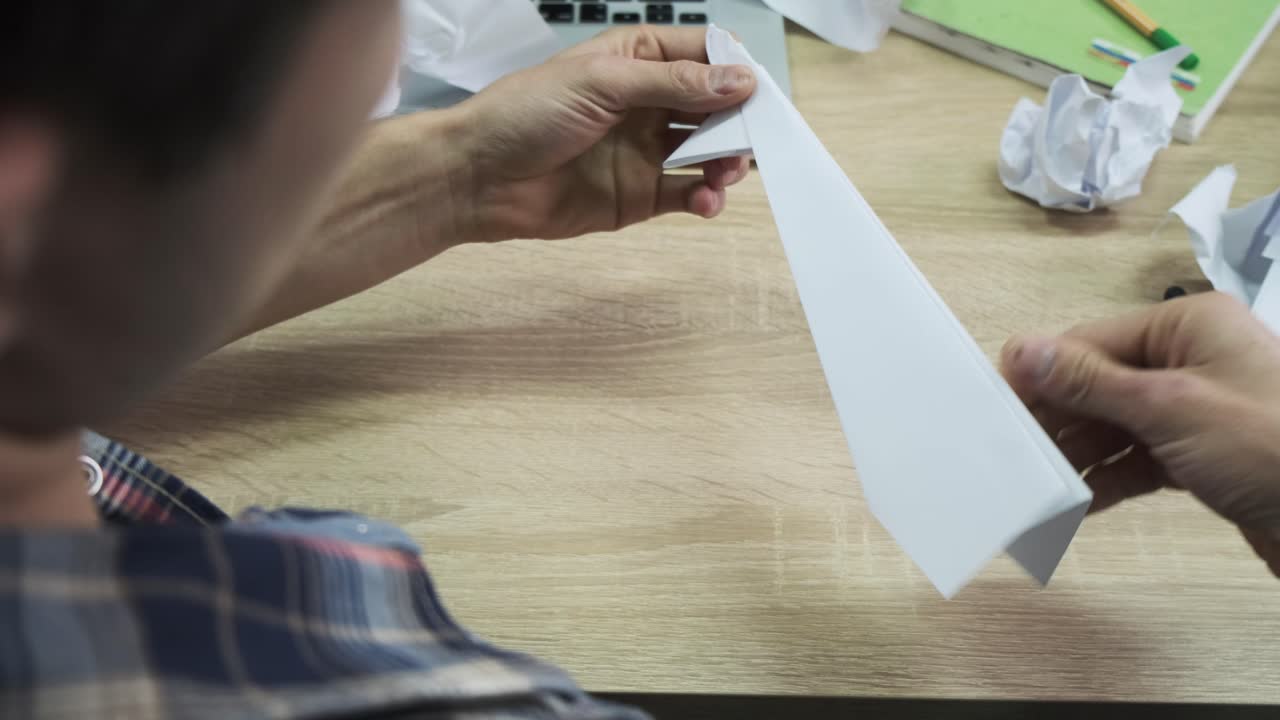 persona haciendo un avión de papel en un escritorio