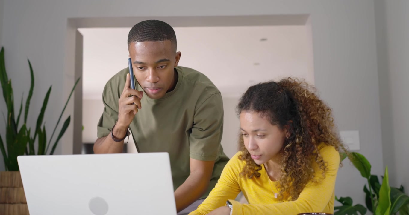 Couple, African American man taking phone call and holding papers, guiding woman on laptop at home