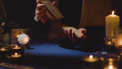 close up of woman shuffling or cutting cards for tarot reading on candlelit table 3