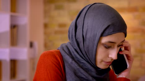 closeup shoot of young attractive muslim female employee in hijab responding to a phone call while typing on the laptop indoors in the office