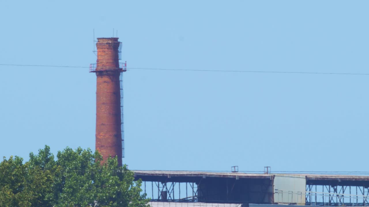 Distant view of abandoned metal melting factory red brick chimney in sunny summer day without clouds, medium shot from a distance