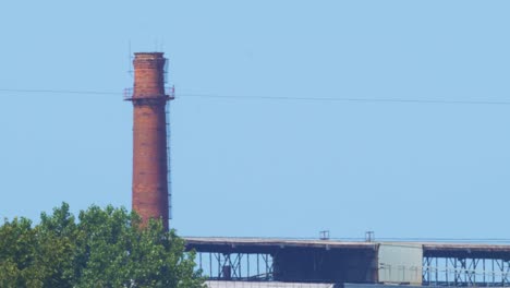 distant view of abandoned metal melting factory red brick chimney in sunny summer day without clouds, medium shot from a distance