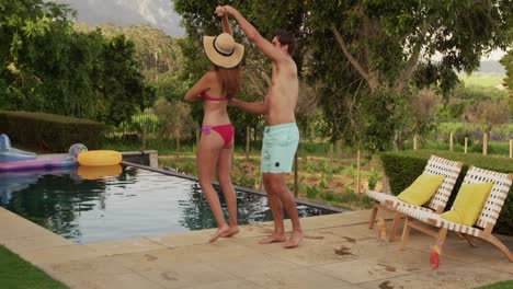 feliz pareja caucásica bailando cerca de la piscina durante un día soleado