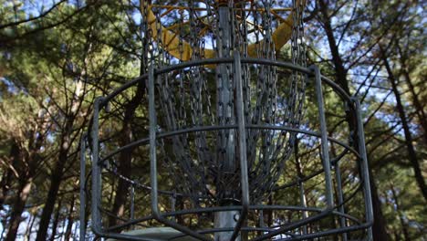 una toma de primer plano de un disco de golf que se arroja rápidamente a una canasta de oro en medio de un bosque