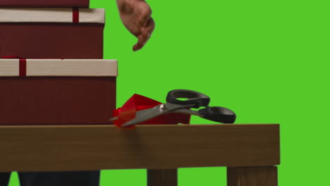 Close-Up-Of-Man-Picking-Up-Gift-Wrapped-Presents-In-Boxes-Decorated-With-Ribbon-On-Table-Shot-Against-Green-Screen-1