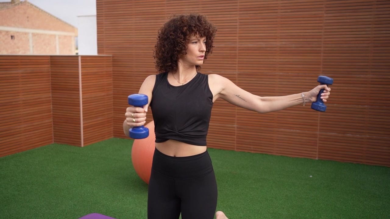 A woman is exercising with dumbbells on a yoga mat outdoors enjoying nature and staying fit