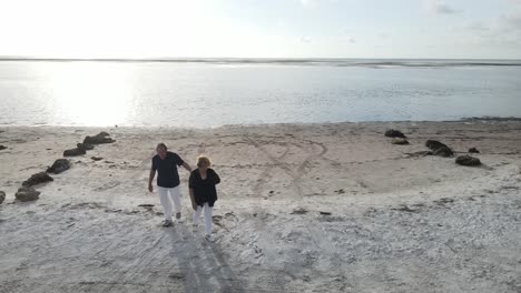 aerial of a loving senior citizen couple walking to leave the beach together, kissing at the last moment