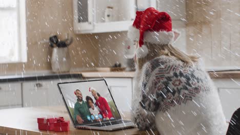 Animación-De-Nieve-Cayendo-Sobre-Una-Mujer-Caucásica-Con-Sombrero-De-Papá-Noel-En-Una-Videollamada-Portátil-Con-Su-Familia