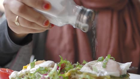 mujer añadiendo sal a un plato de huevos cocidos y aguacate