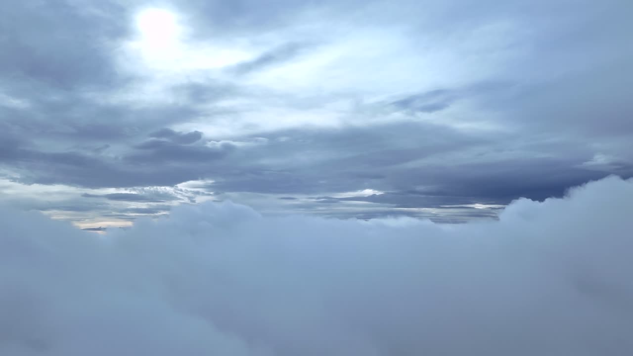 An immersive cockpit view entering a layer of ethereal stratus clouds in a dramatic winter sky, with a faded sun veiled by a layer of clouds