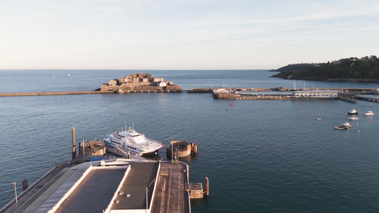 Porto di St Peter Port, Guernsey, Isole del Canale. Filmato lento in avanti sopra il traghetto al terminal direttamente verso Castle Cornet nel sole del tardo pomeriggio in una giornata calma con vista sulla costa