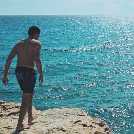 man jumping off cliff into the ocean.