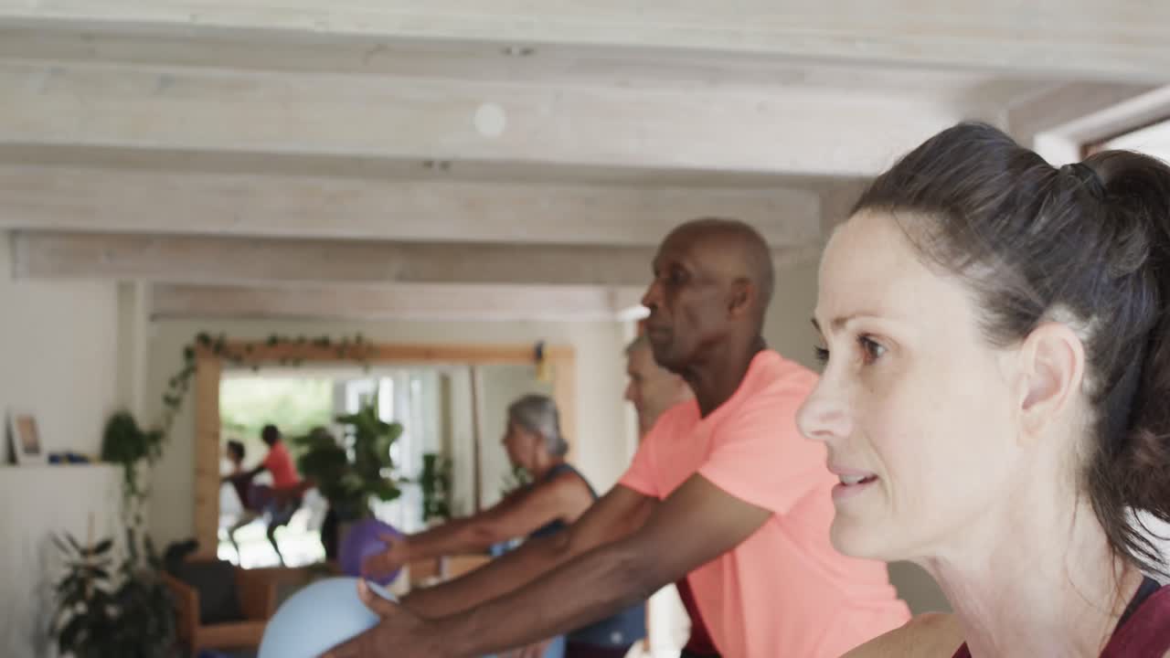 Diverse Senioren trainieren mit Bällen mit weiblicher Pilates-Trainerin, unbearbeitet, in Zeitlupe