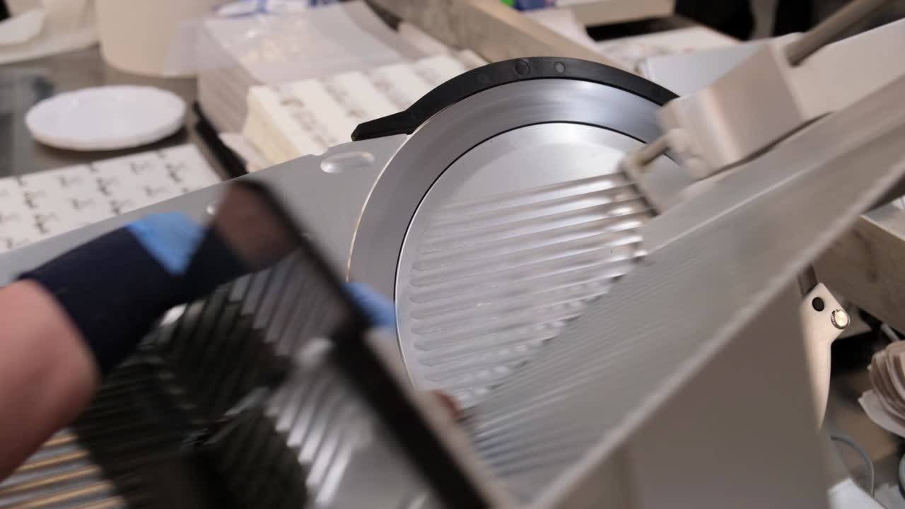 продавец в супермаркете режет колбасы с помощью автоматического большого ножа.