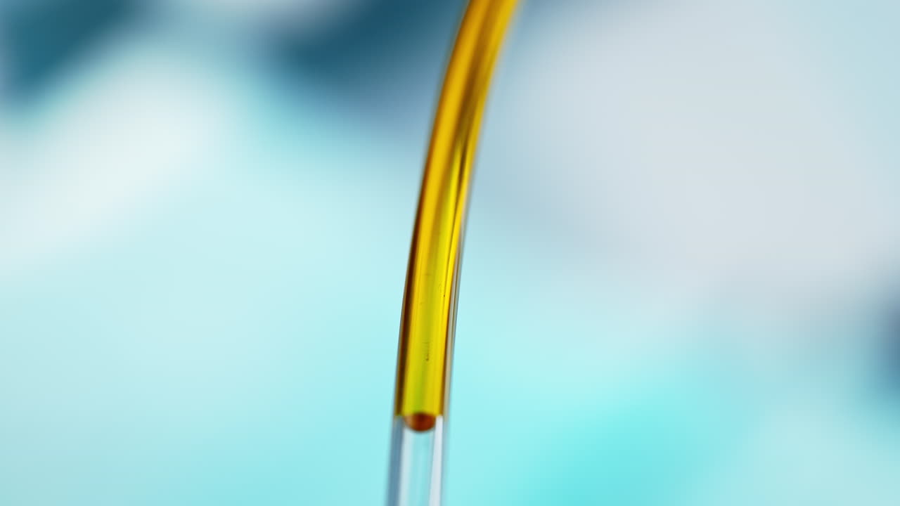 투명한 튜브를 통해 비타민을 주입합니다. 흐릿한 파란 병원 배경에서. 거시 및 느린 동작으로 노란 액체.